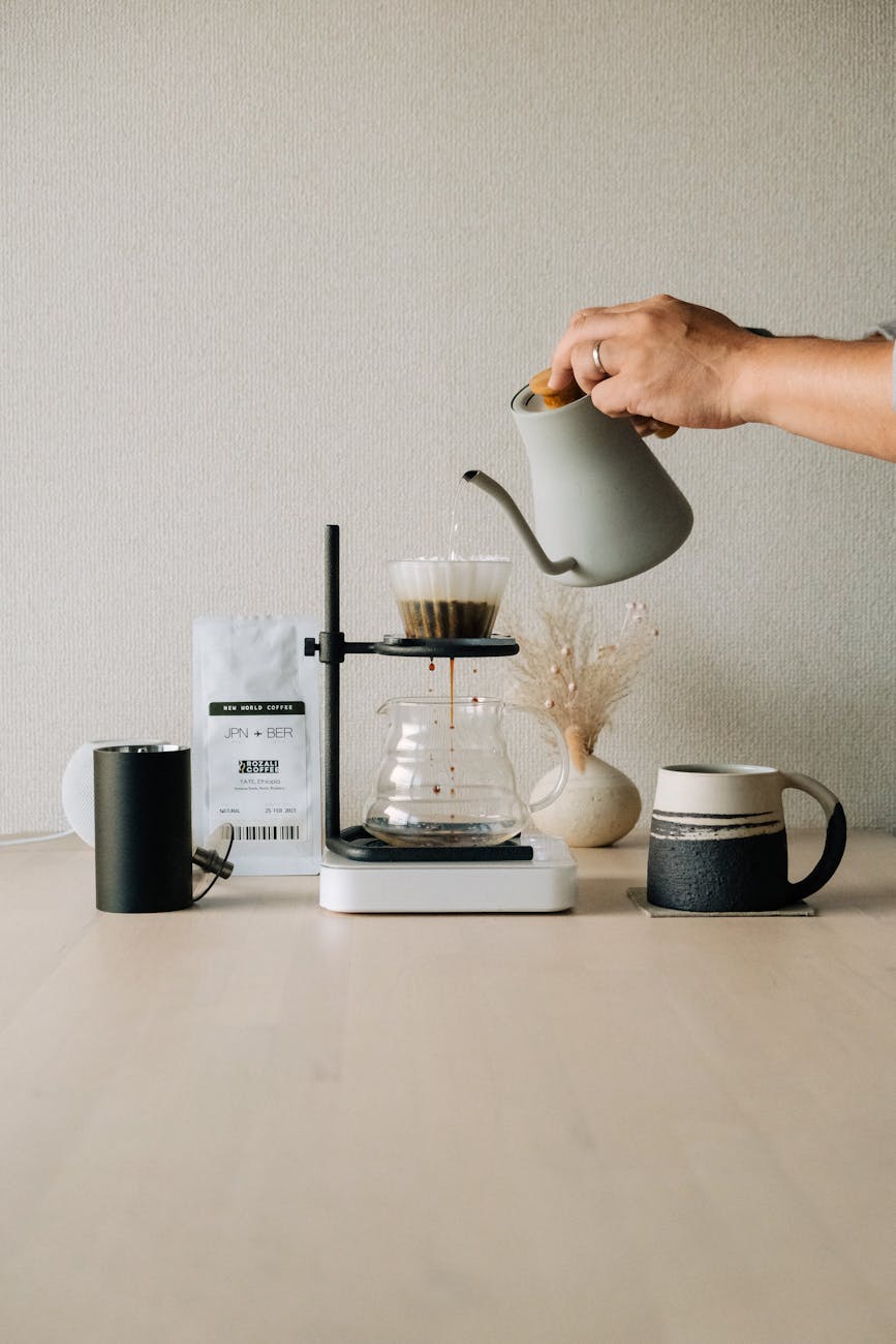 A pour-over setup with a premium coffee scale, gooseneck kettle, and V60 dripper, water being poured over coffee grounds, steam rising, soft morning light, rustic kitchen background, professional photography