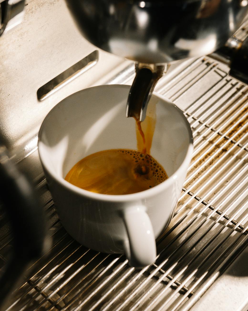 A close-up shot of a barista pulling a perfectly flowing espresso shot into a demitasse cup on a scale, showing the measurement of liquid espresso yield.