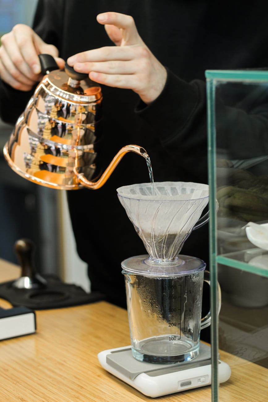A close-up of filtered water being poured from a Brita pitcher into a coffee machine's water reservoir, illustrating the use of filtered water for maintenance.