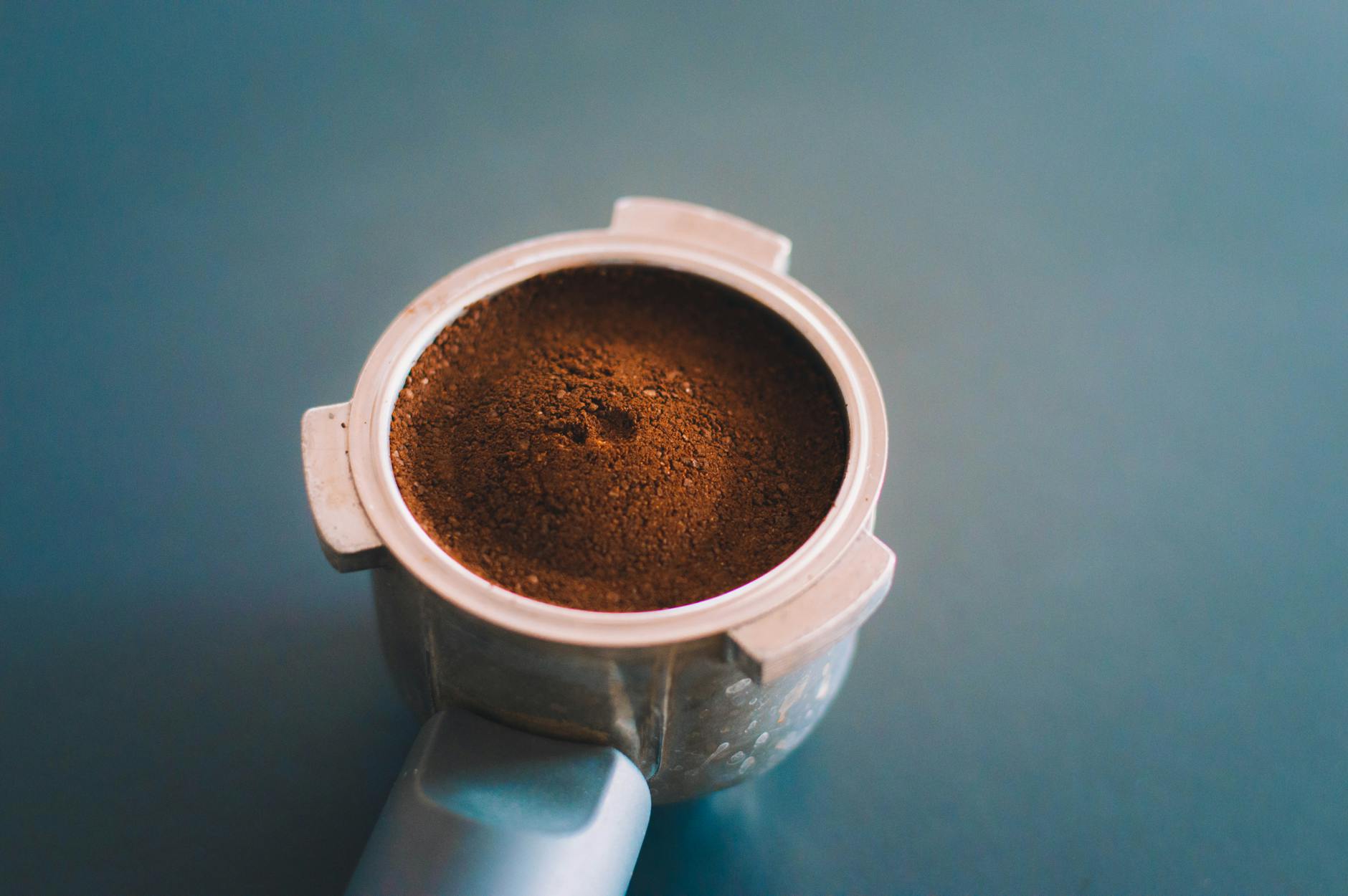 A close-up of freshly ground coffee pouring into an espresso portafilter, with whole roasted coffee beans visible in the background, emphasizing freshness and quality.