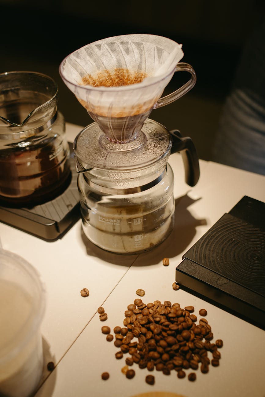 A perfectly brewed pour-over coffee in a clear glass mug, with a bag of recommended specialty coffee beans next to it. The coffee has a golden crema, and the beans are whole and vibrant, suggesting freshness and quality.