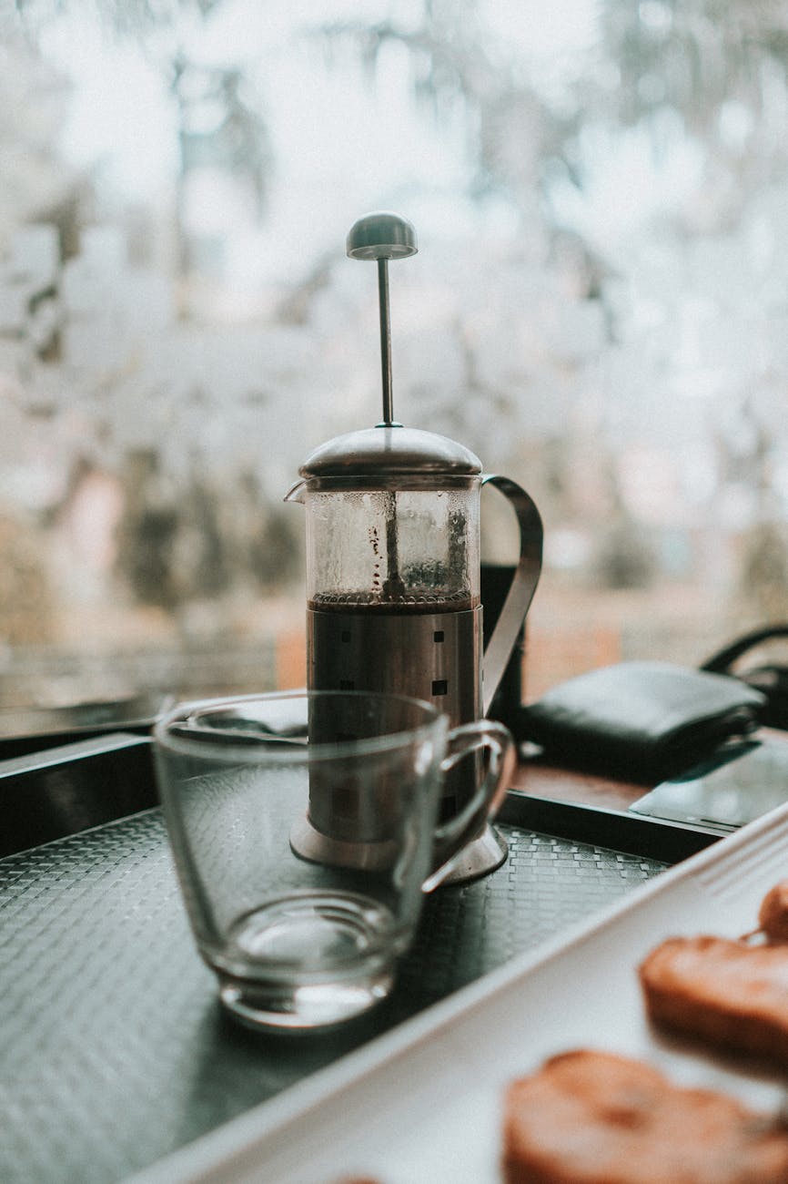 Close-up of a French Press with coffee grounds fully immersed in hot water, showing the steeping process before plunging. Steam rises gently.