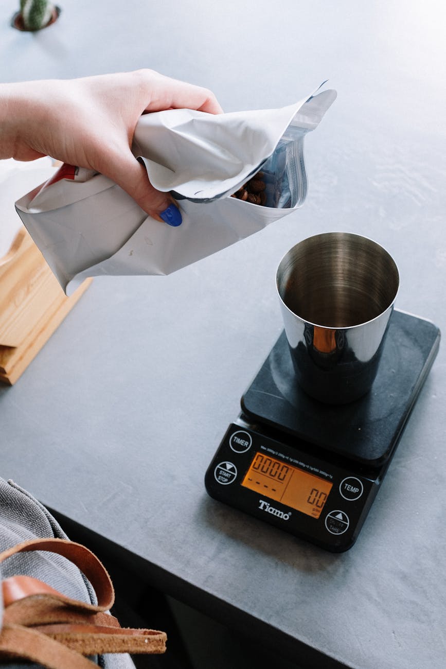 A close-up shot of a barista carefully weighing coffee beans on a sleek, digital premium coffee scale, with an espresso machine blurred in the background, cinematic lighting, shallow depth of field, high quality, photorealistic