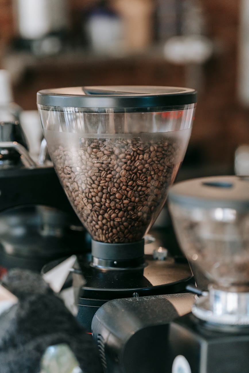 A close-up shot of hands adjusting the grind setting dial on a high-quality electric burr coffee grinder, with coffee beans visible in the hopper. A digital scale with coffee grounds is in the background.