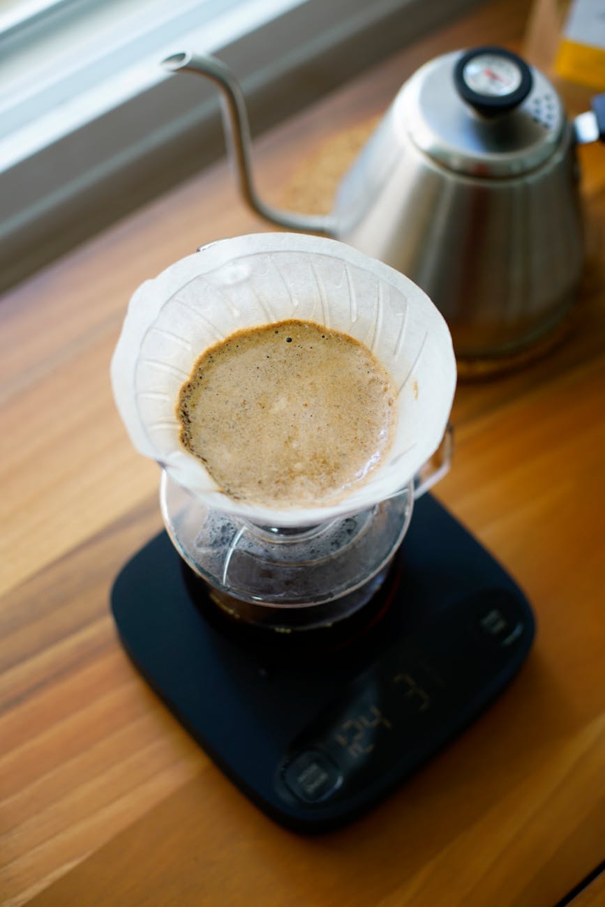 Hands placing coffee grounds into a pour-over cone on a digital scale, illustrating the importance of precise measurement for coffee ratios.